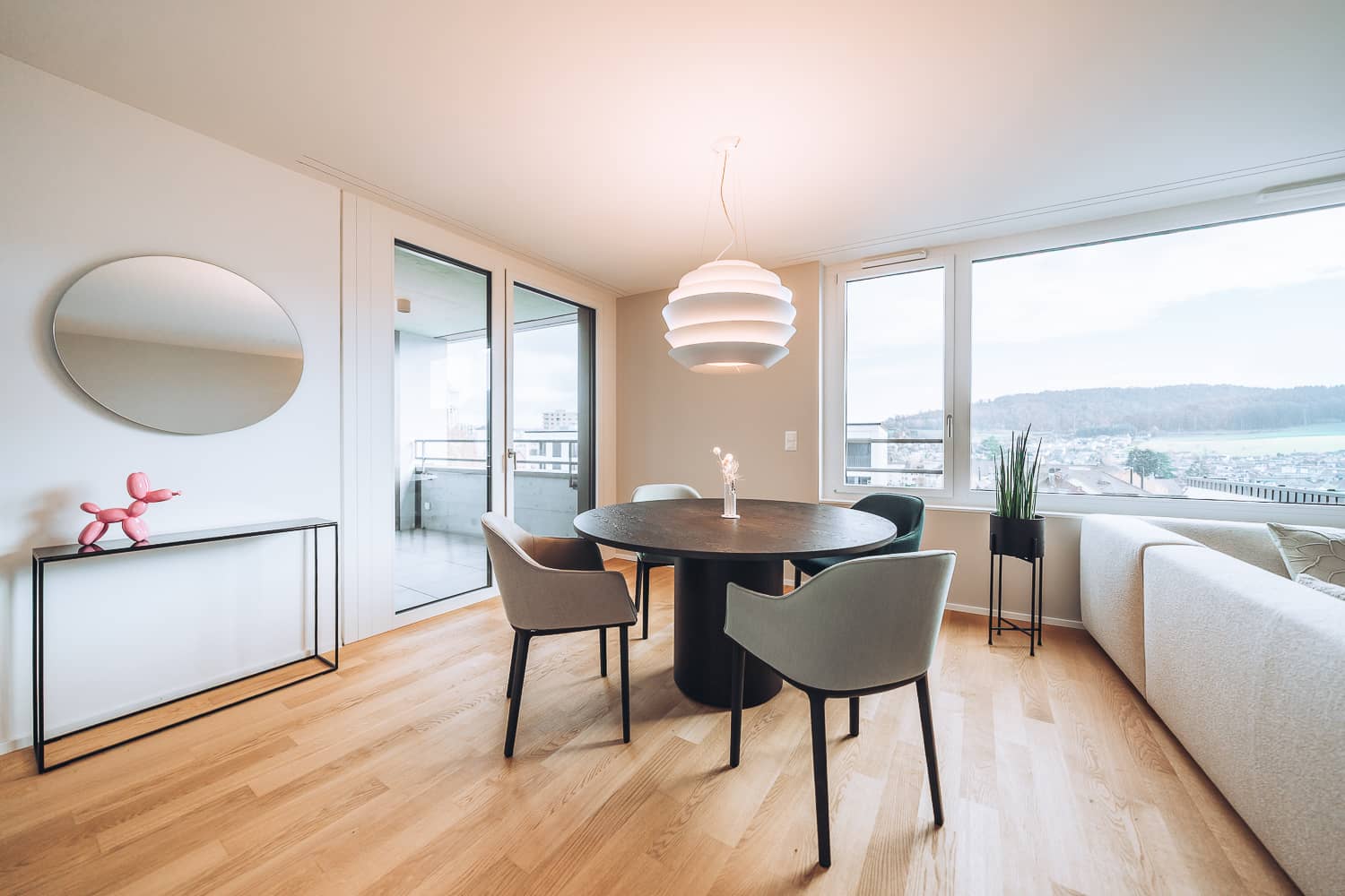 Neben einer Esszimmergruppe mit H&auml;ngeleuchte steht ein Sideboard an der Wand, &uuml;ber welchem ein ovaler Spiegel h&auml;ngt
